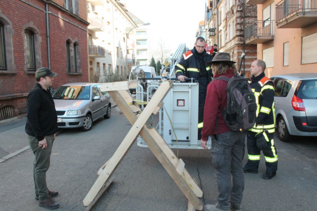 Helfer und Feuerwehr beratschlagen, wie sie Gestell und Nest auf das Dach bekommen.
