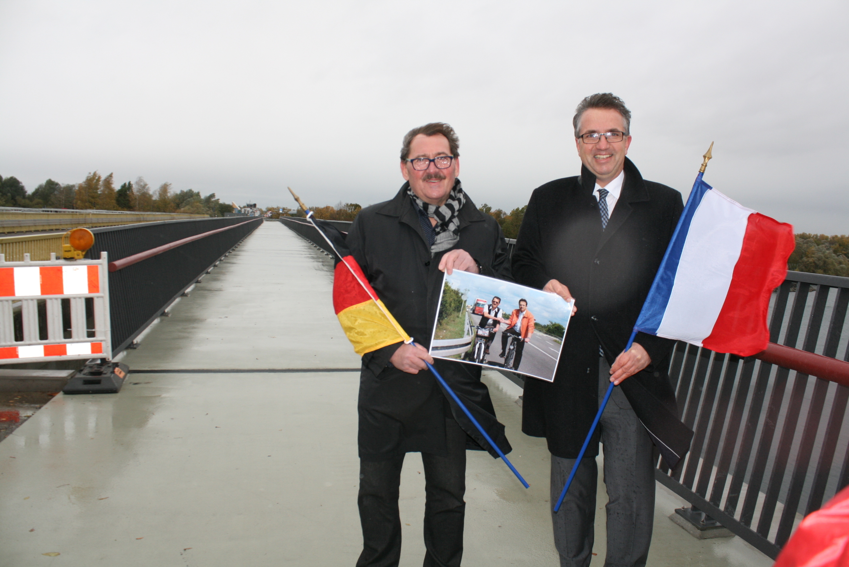 Die ersten 144 Meter der Geh- und Radwegbrücke sind freigeben: Hubert Hoffmann und Michael Welche (r.) erinnern mit einem Foto an den Beginn des Projekts vor neun Jahren.