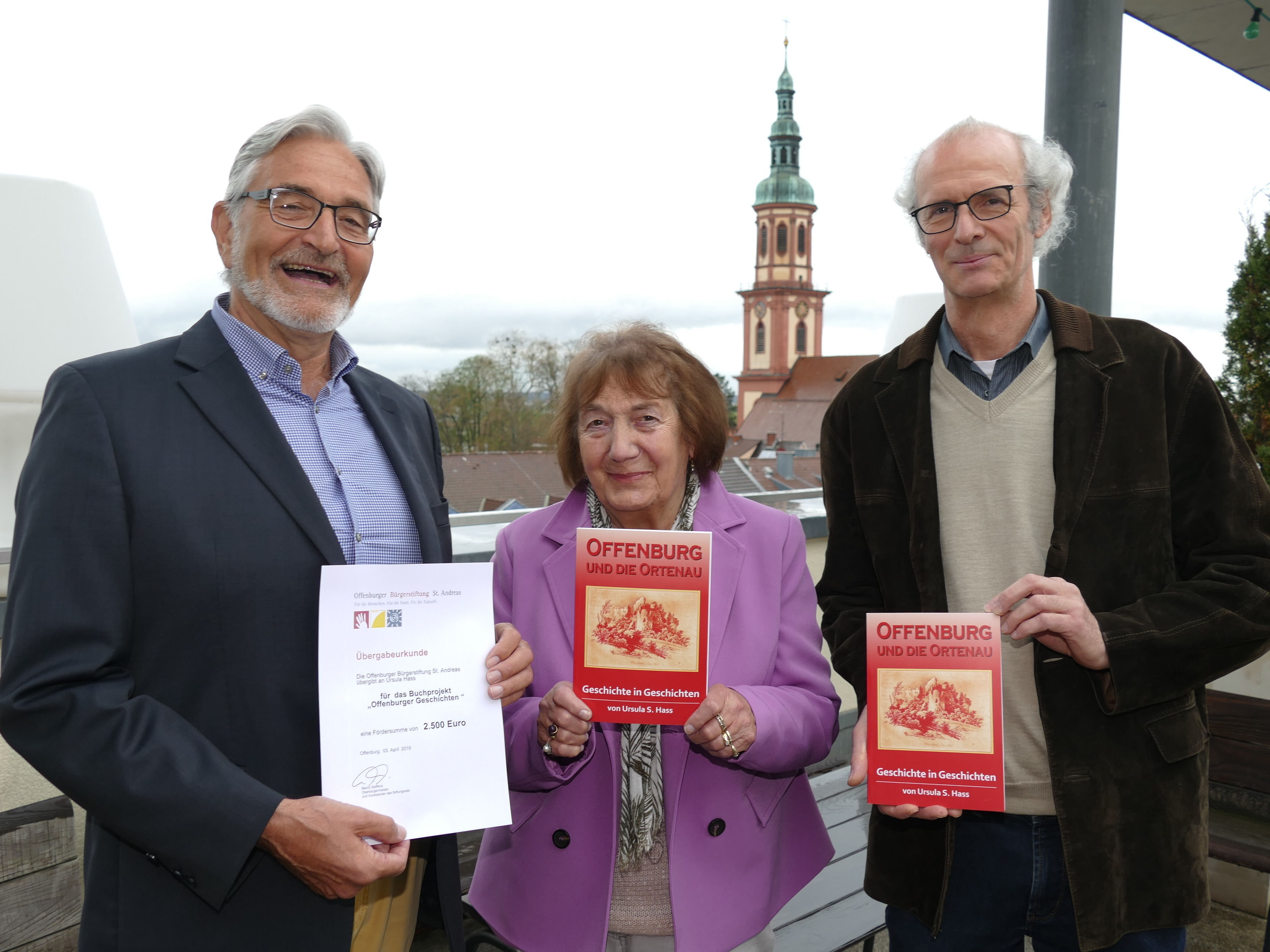 Über den Dächern von Offenburg präsentiert Ursula Hass ihr Geschichtenbuch, daneben (links) Bernhard Schneider (Bürgerstiftung) und Georg Huber (Druckerei Huber).