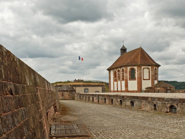 Die Kapelle auf dem oberen Plateau. In ihr befand sich auch die Zisterne.  Ihr Standort nahe am Wall, ist kein Zufall, da es galt das eine weihin sichtbare Kirche und ihre unmittelbare Umgebung nicht beschossen werden. Daher überstand die Kapelle die Angriffe fast unbeschädigt. Im Innenraum der Kapelle seht ein großes Relief der Bitscher Festung. Auf dem Sockel den man rechts sieht stand das Gebäude der großen Kaserne. | Foto: Alfred Schramm