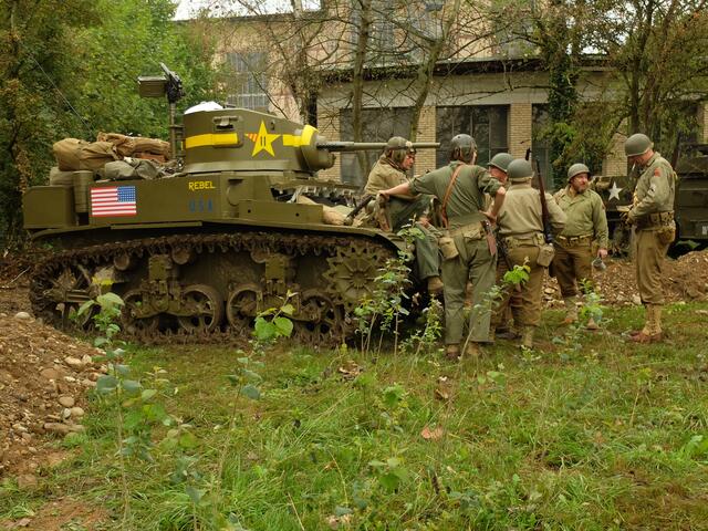 Darsteller, in amerikanischen Uniformen, bei der Lagebesprechung vor einem M3 Stuart.
Der M3 Stuart war ein leichter US-amerikanischer Panzer, der im Zweiten Weltkrieg ab 1941 zum Einsatz kam. Er wurde wegen seiner Schnelligkeit hauptsächlich zur Aufklärung eingesetzt, wobei er sich gut bewährte. Für den Einsatz gegen Kampfpanzer war das Fahrzeug zu schwach gepanzert, aber sehr wirksam gegen Infanterie.
 | Foto: Alfred Schramm