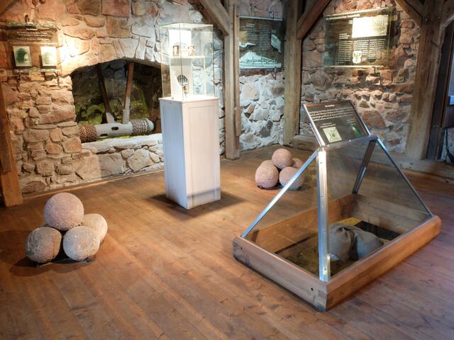 Der Eingangsbereich der Torhalle, wurde durch ein Fallgitter geschützt, hinter diesem war noch ein Flügeltor angebracht. 
In der 1. Etage sind zu sehen der sogenannte "Totschläger". Das war eine Öffnung durch die, die Männer der Turmbesatzung Sandsteinkugeln auf die eingedrungenen Feinde geworfen haben. Zerschellten diese Kugeln auf dem harten Boden, gab es Splitterwirkungen und sorgte bei den feindlichen Soldaten, für Verletzungen. Die zu sehenden Steinkugeln, stammen aus der Zeit zwischen dem 13. bis 15. Jahrhundert. Weiterhin sieht man die Umlenkwalze des Fallgitters sowie das Modell eines solchen. Schautafeln erläutern die Funktion des Turmes. | Foto: Alfred Schramm