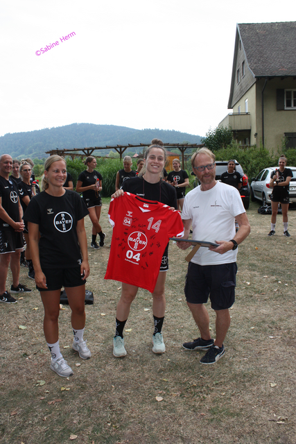 Anne Krüger und Mariana Ferreira Lopes (von links nach rechts) übergeben Hartmut Bruch ein Mannschaftsbild und ein handsigniertes Trikot vom TSV Bayer Leverkusen 04 &gt;&gt;Werkselfen&lt;&lt; | Foto: ©Sabine Herm