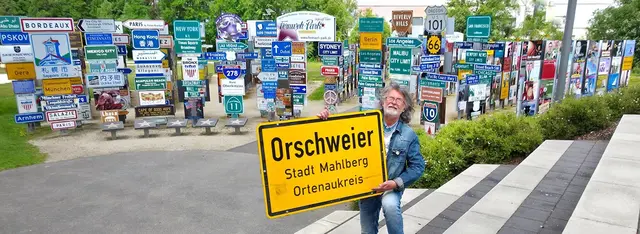 Fernwehpark-Initiator Klaus Beer vor der Panorama-Schilder-Weltkulisse, die Abteilung der „lustigen Ortsnamen“ | Foto:  Fernweh-Park