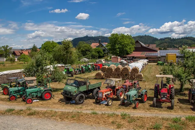 Grüne und rote Oldtimer-Traktoren sowie ein Unimog stehen auf einer Wiese am Ortsrand, im Hintergrund die bewaldeten Hügel der Ortenau.