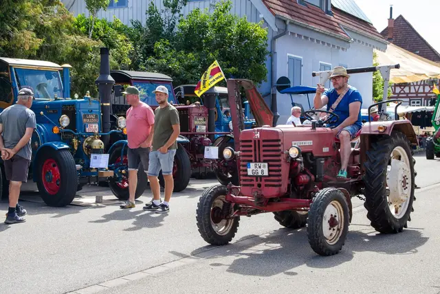 Historischer roter Oldtimer-Traktor rollt beim Unimog- und Schlepper-Treffen durch die Biberacher Ortsmitte, daneben blaue Lanz-Bulldog-Schlepper und Zuschauer am Straßenrand.