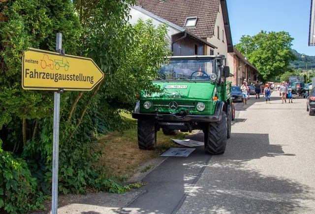 Grüner Mercedes-Unimog parkt neben einem gelben Wegweiser zur „weiteren Fahrzeugausstellung" beim Biberacher Treffen.