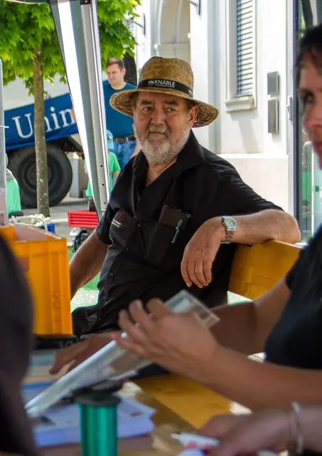 Festbesucher mit Strohhut sitzt im schattigen Festbereich des Unimog- und Schlepper-Treffens an einem Tisch, vor sich ein kühles Getränk.