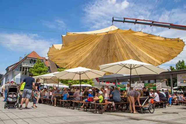 Gut gefüllte Bierbänke im Festbereich vor dem Rathaus: Der große Lastenfallschirm und weitere Sonnenschirme spenden den zahlreichen Gästen Schatten.