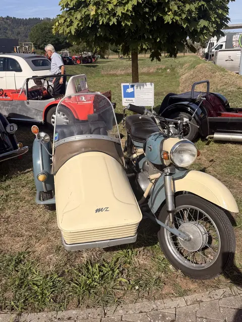 Motorrad mit cremefarbenem Beiwagen, dahinter Oldtimer-Autos.