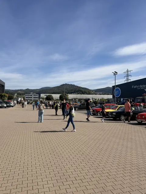 Besucher gehen zwischen geparkten Oldtimern über das Ausstellungsgelände.